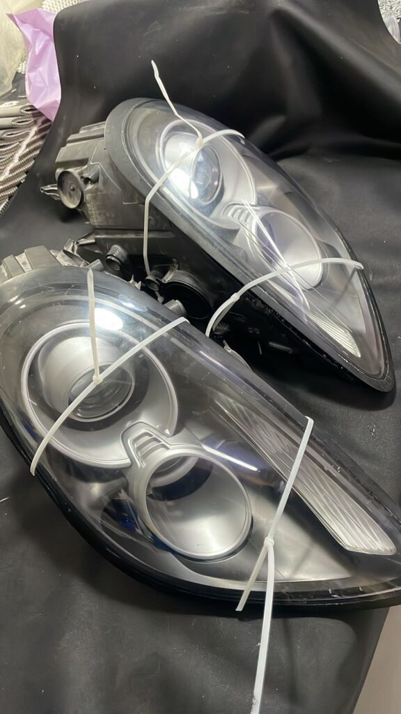Reassembled Porsche Cayman headlight secured with cable ties to hold the lens in place while silicone sealant cures – part of retrofit process at DSUS Auto Care Center Dubai.