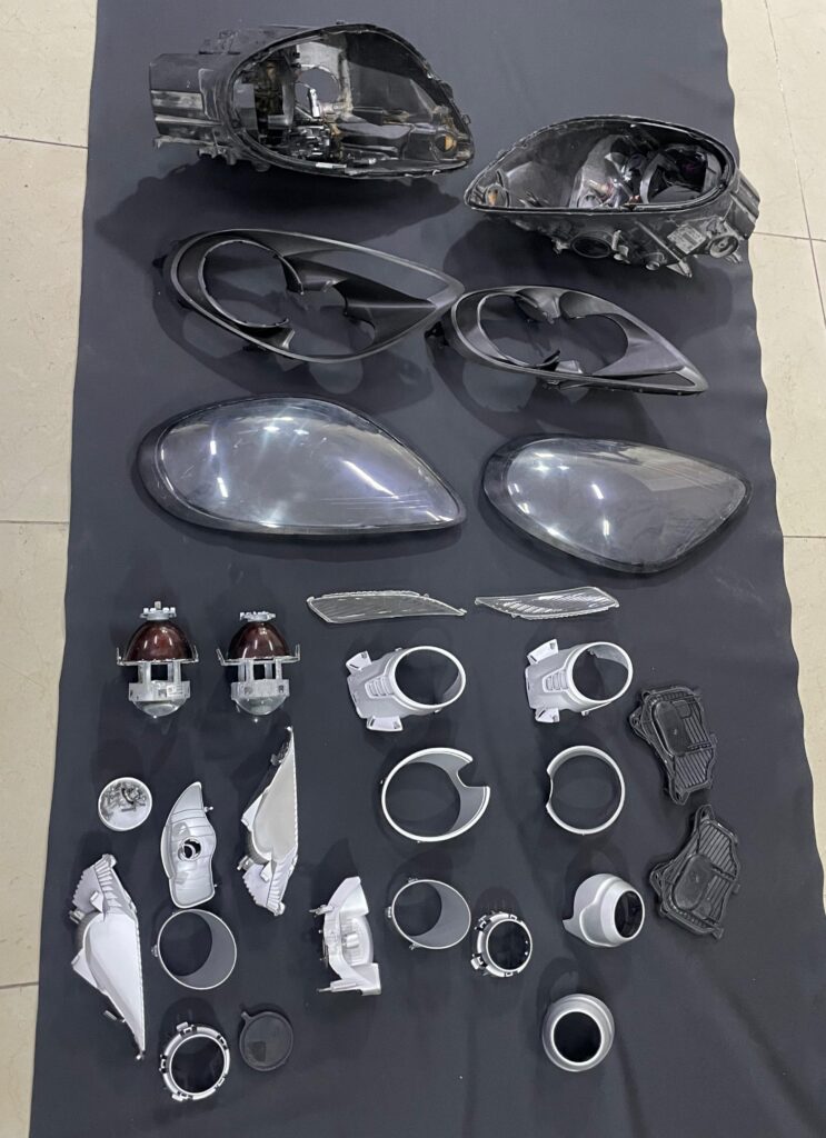 “Disassembled headlight components of a 2014 Porsche Cayman, showing internal and external parts prepared for retrofit and restoration.
