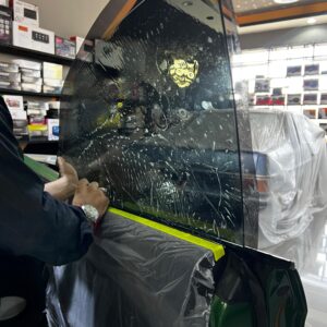 Technician applying tint film to a car window in a workshop.
