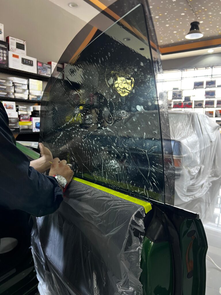 Technician applying tint film to a car window in a workshop.